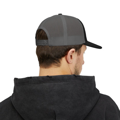 A person is seen from behind, wearing a black trucker cap with a charcoal mesh back. They are also dressed in a dark hoodie, and their hair is short and dark, showcasing a casual style.