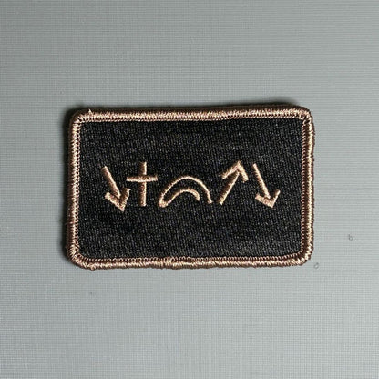 A rectangular black Velcro patch with green and beige embroidery depicting five gospel symbols.