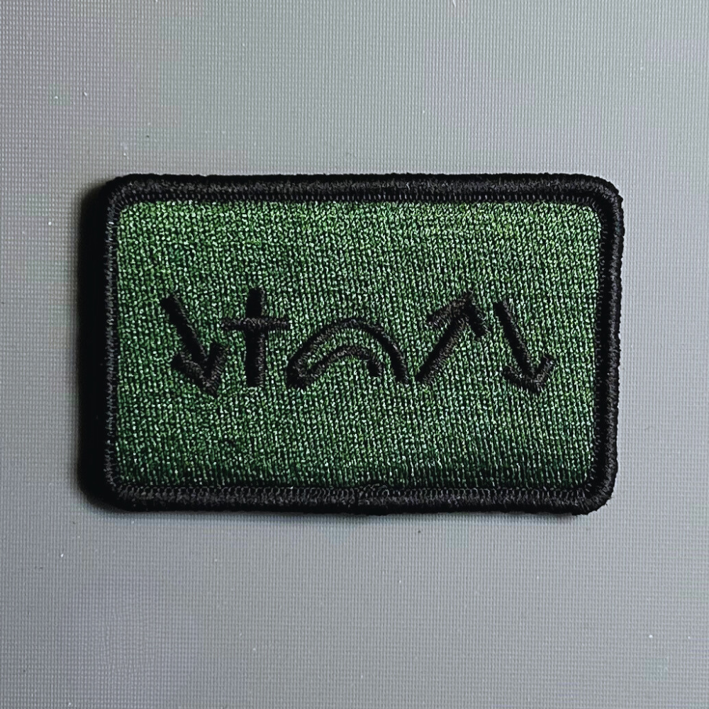A rectangular black Velcro patch with green and beige embroidery depicting five gospel symbols.