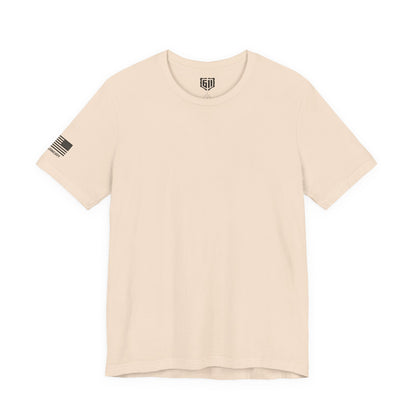Beige t-shirt with a US Flag and logo on the left sleeve against a white background