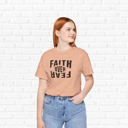 Person wearing a peach t-shirt with 'Faith Over Fear' text against a white brick wall.